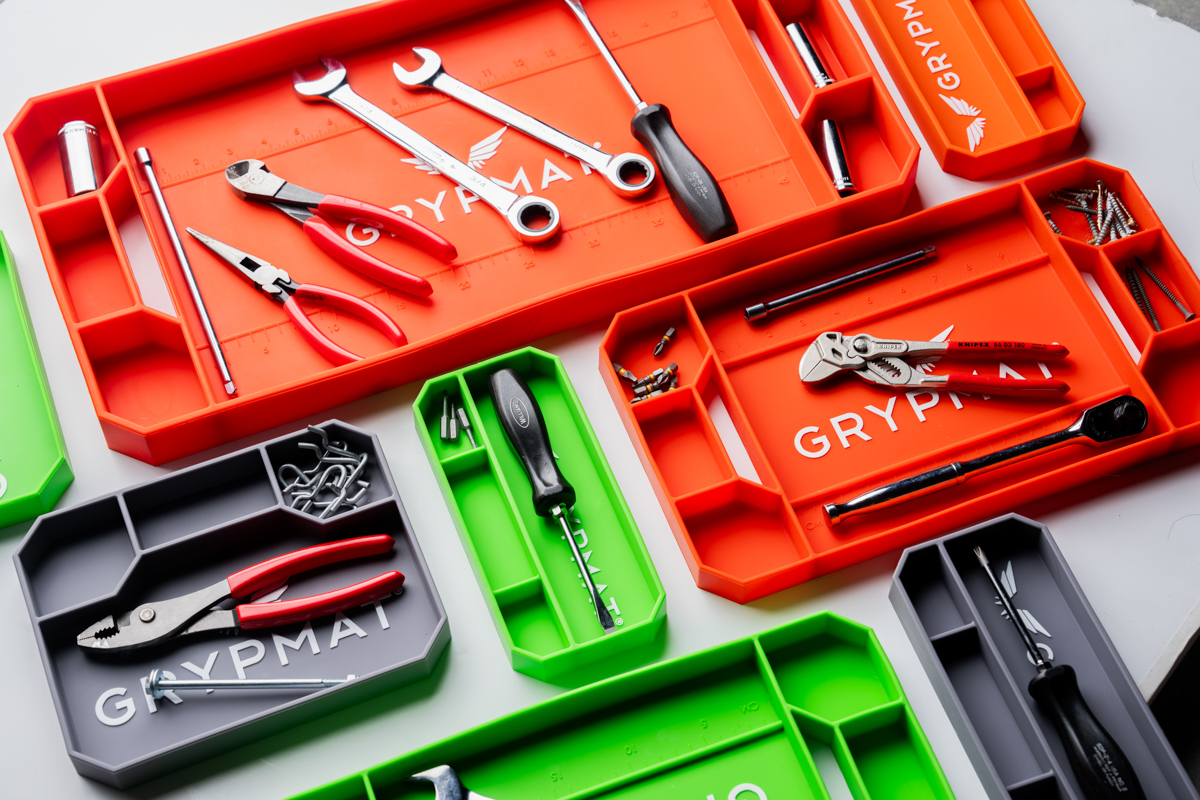 Multiple Grypmat trays in orange, green, and grey filled with tools