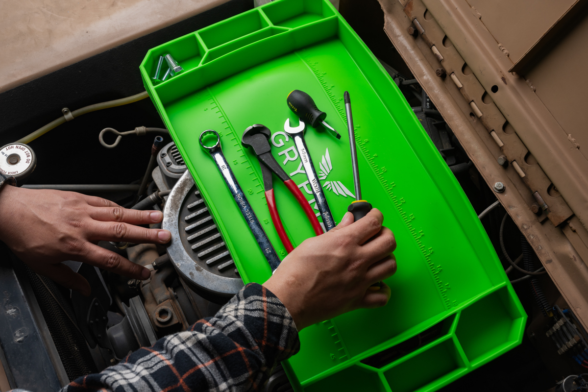 Mechanic selecting a tool from a green Grypmat tray on an engine
