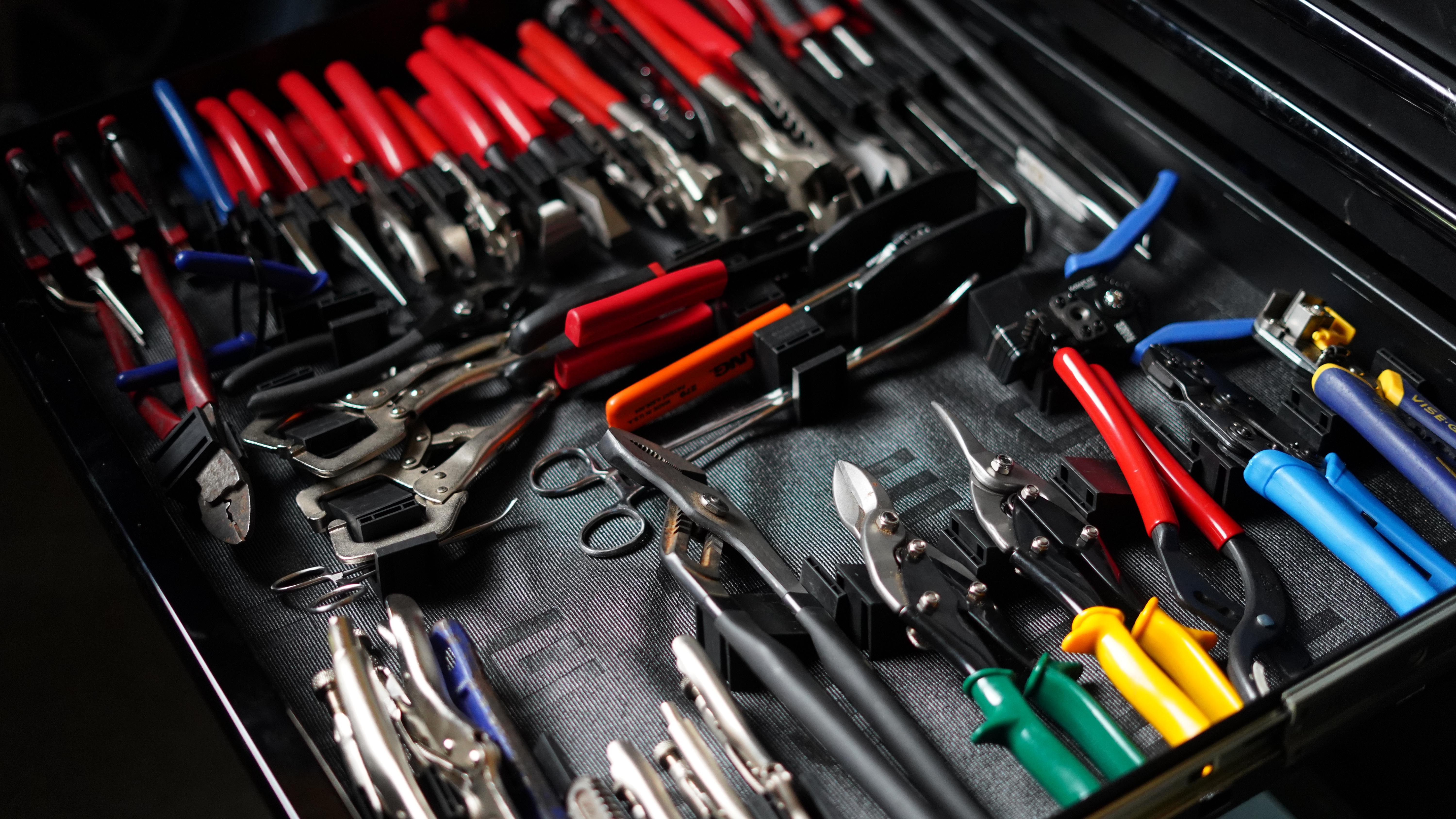 Top-down view of a black tool drawer containing neatly organized red-handled pliers in foam